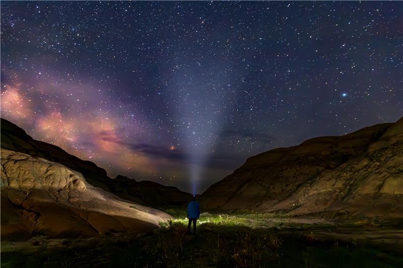 Person standing in a desert canyon at night, shining a flashlight toward a star-filled sky