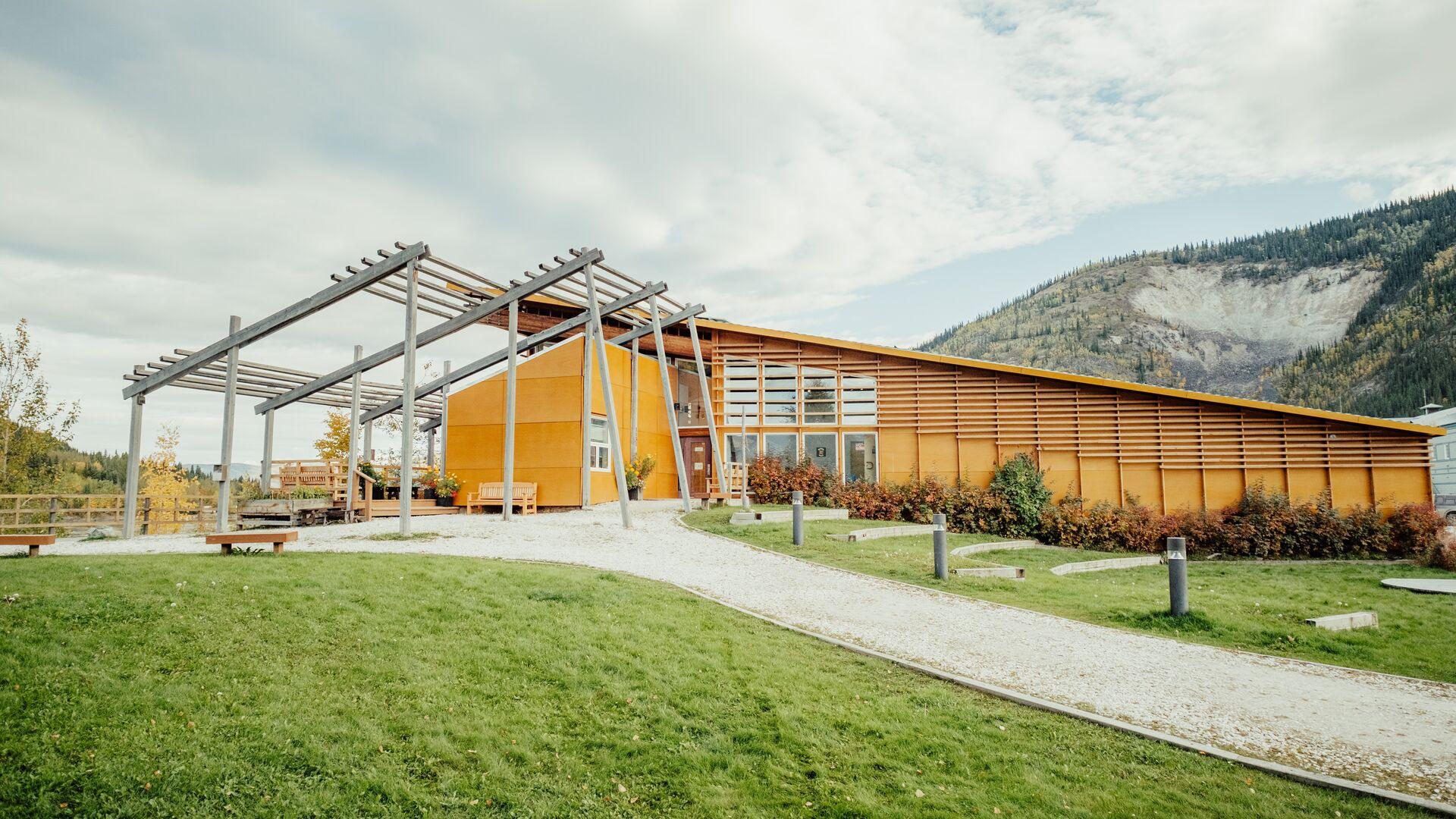 Modern wood-clad building with a landscaped lawn and mountain backdrop.