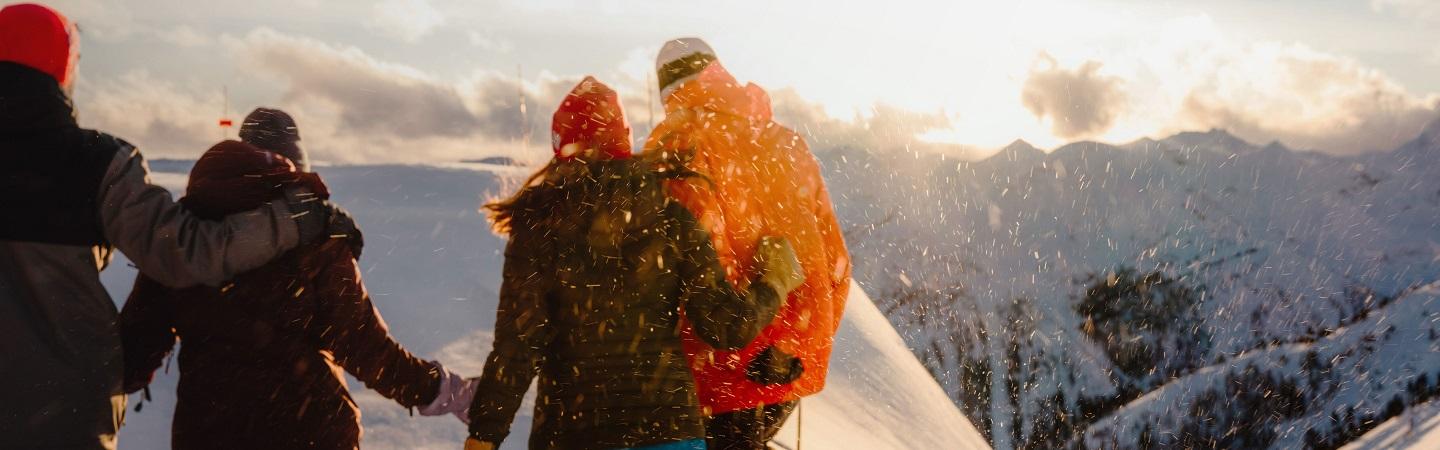 A group of people standing at the snowy peak of a mountain at sunrise.