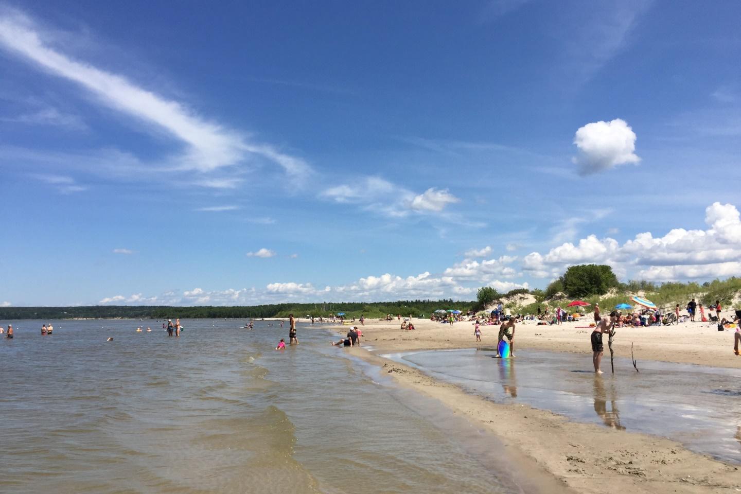 Beach goers walking into the ocean from the white sand on a sunny day.