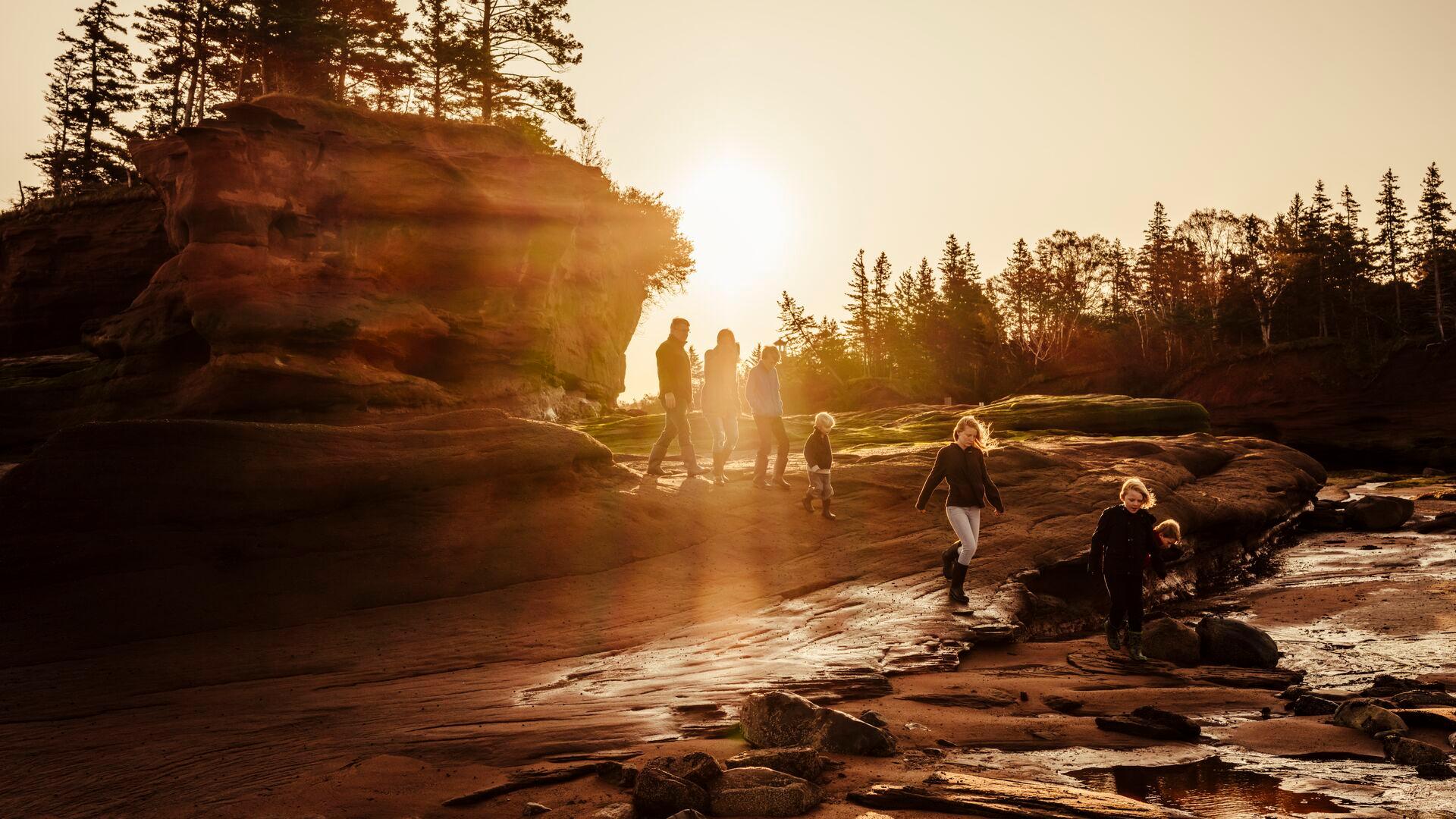 A family plays on tall rock structures at the beach at sunset.