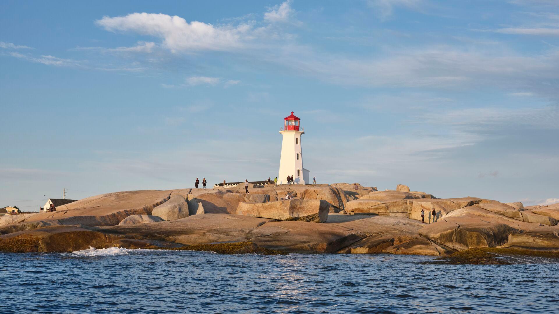 White lighthouse with a red top standing on a rocky coastline beside the ocean