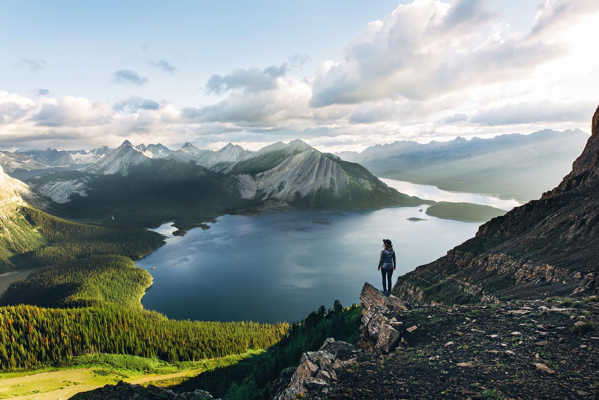 solo hiker stands on rocky outcrop overlooking a lake and mountains