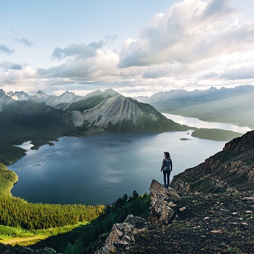 solo hiker stands on rocky outcrop overlooking a lake and mountains
