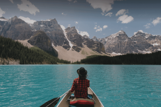 Person canoeing on bright blue water towards mountains.