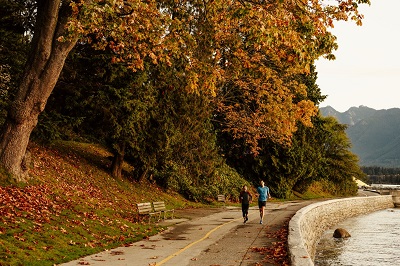 people jogging along the seawall in Stanley Park with trees showing their autumn colours