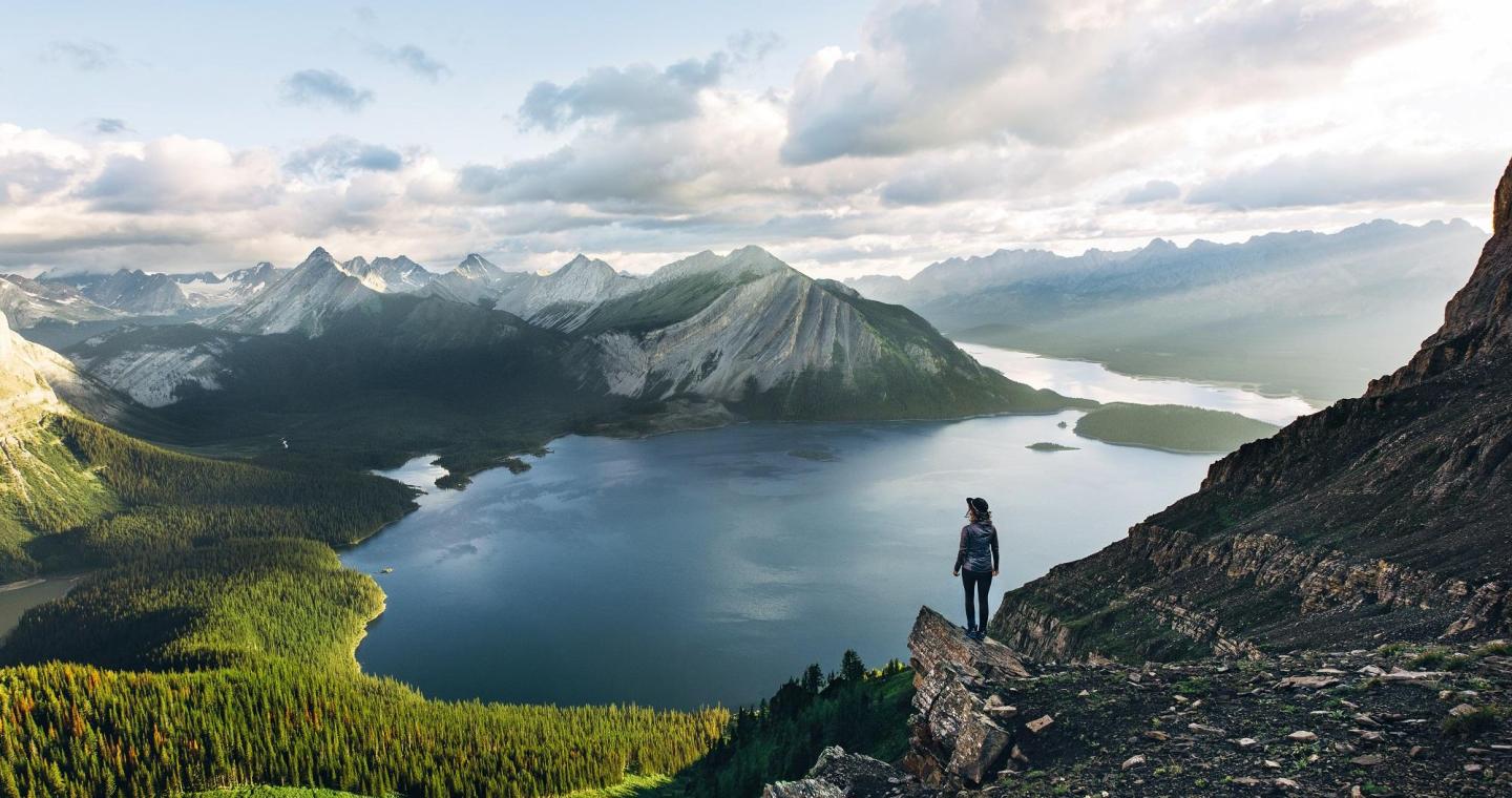 solo hiker stands on rocky outcrop overlooking a lake and mountains