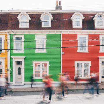 Des gens floutés marchent devant des bâtiments colorés.